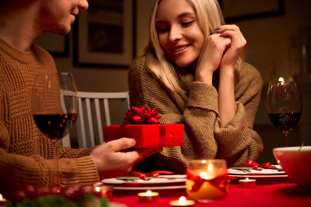Boyfriend holding gift making present to girlfriend having romantic dinner date.