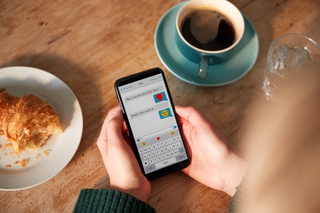 Close Up Of Woman Looking At Messages Arranging Romantic Date On Mobile Phone Messaging App In Cafe
