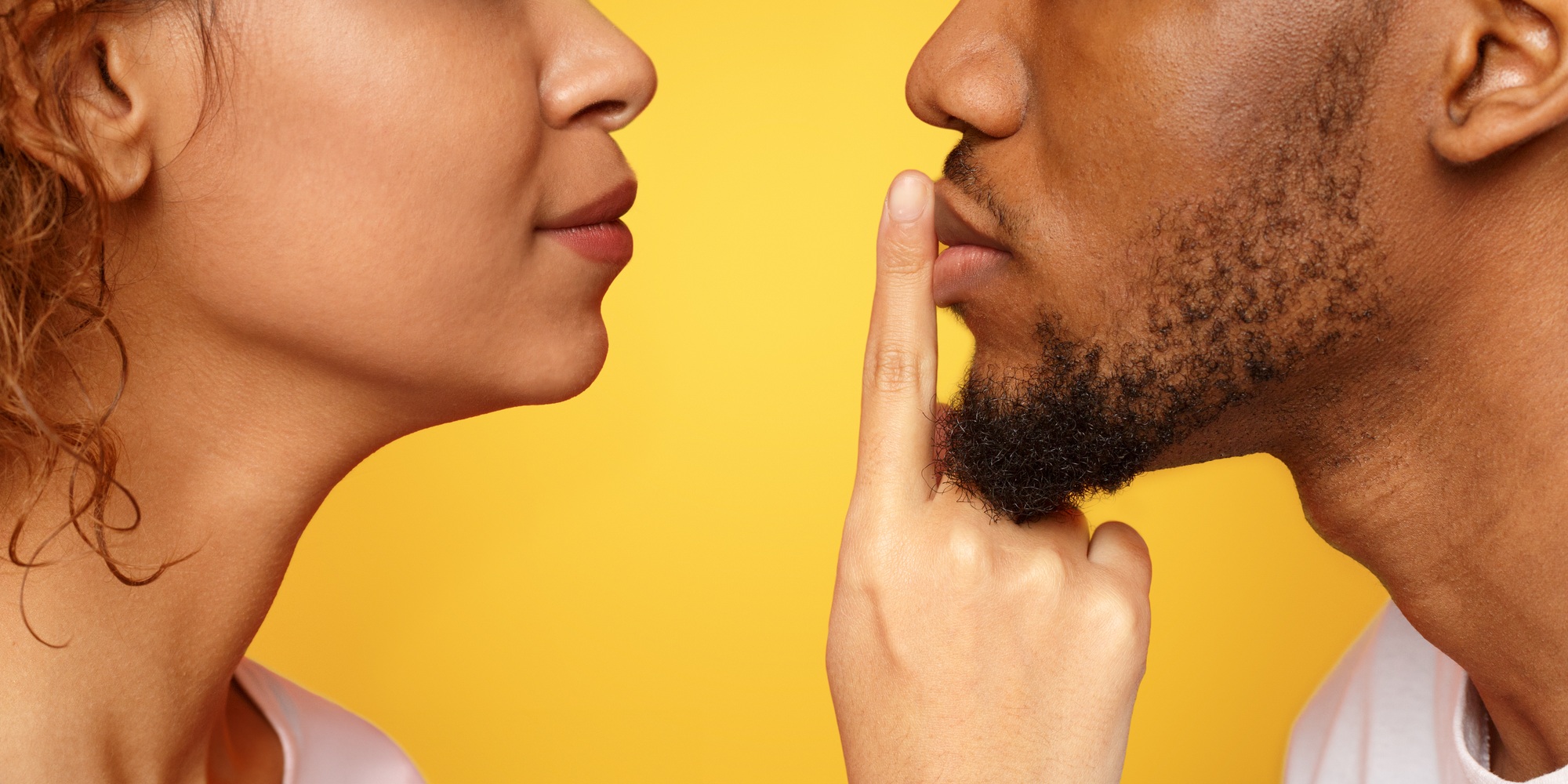 Profile of mysterious woman touching male lips with finger